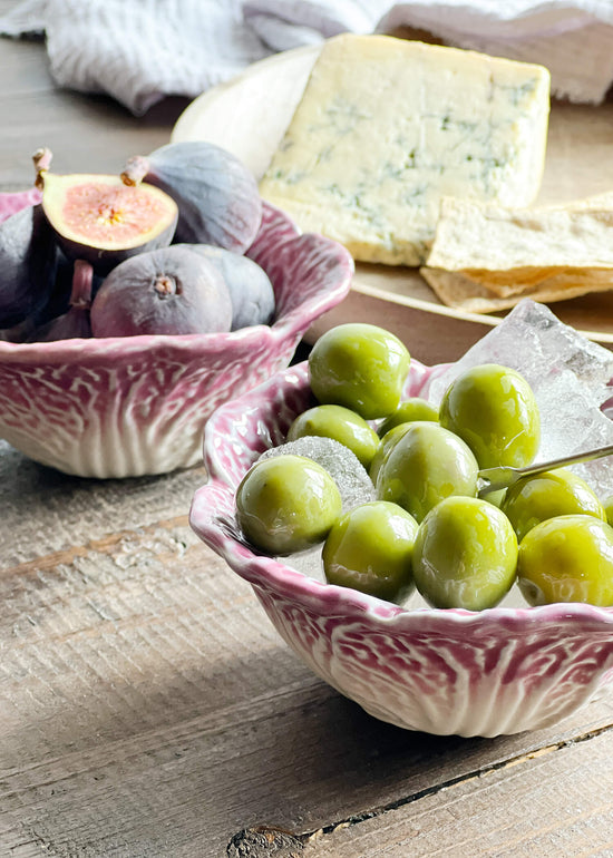 Side view of ceramic cabbage bowls holding olives and figs with cheese in the background